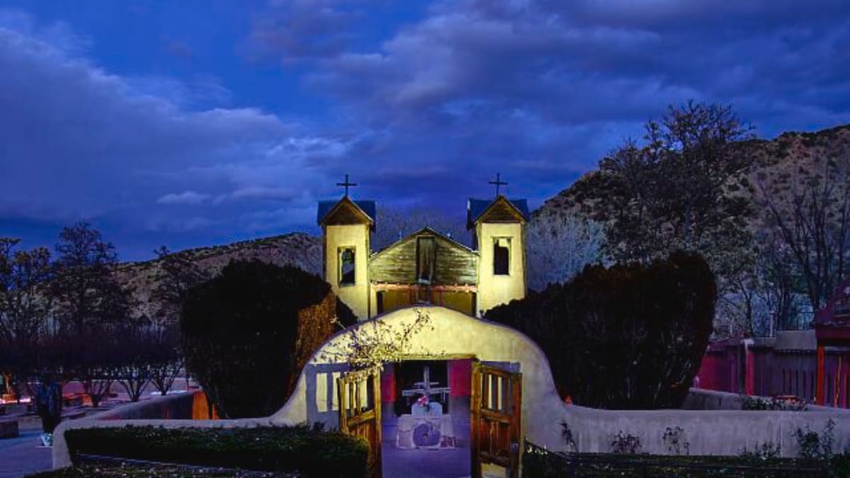 The adobe twin-towered El Santuario de Chimayo church glows at dusk in its New Mexico mountain village worship site.