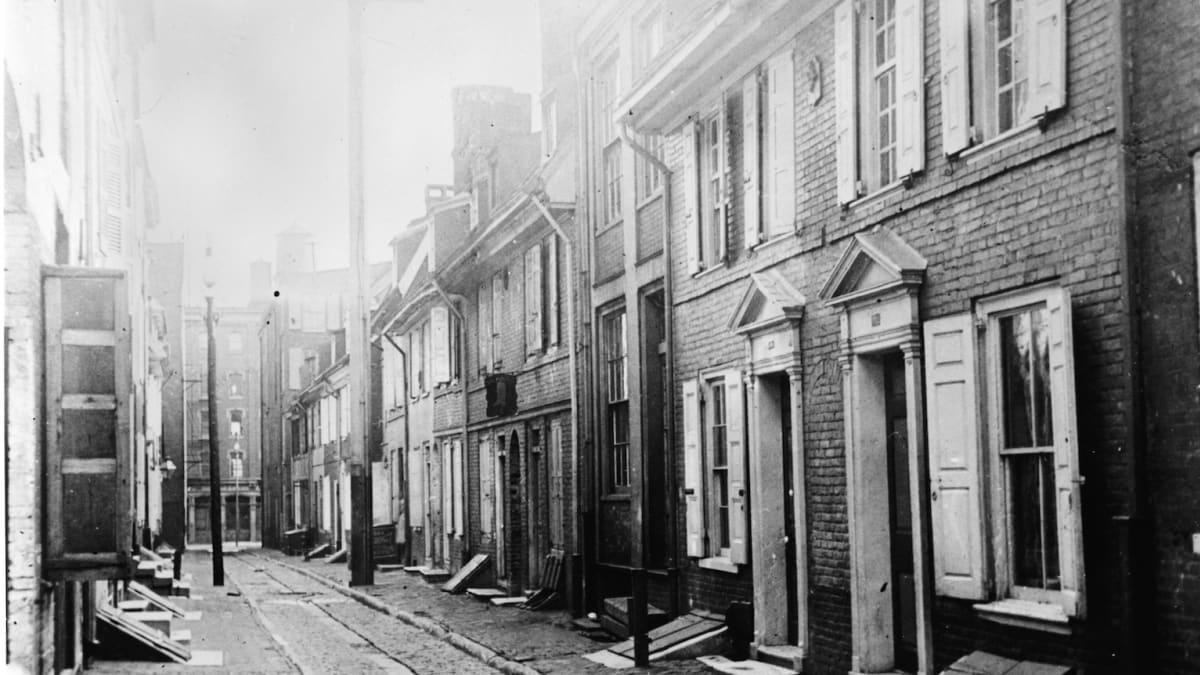 A historic photograph of the cobblestone lane and colonial brick rowhouses of Elfreth's Alley in Philadelphia
