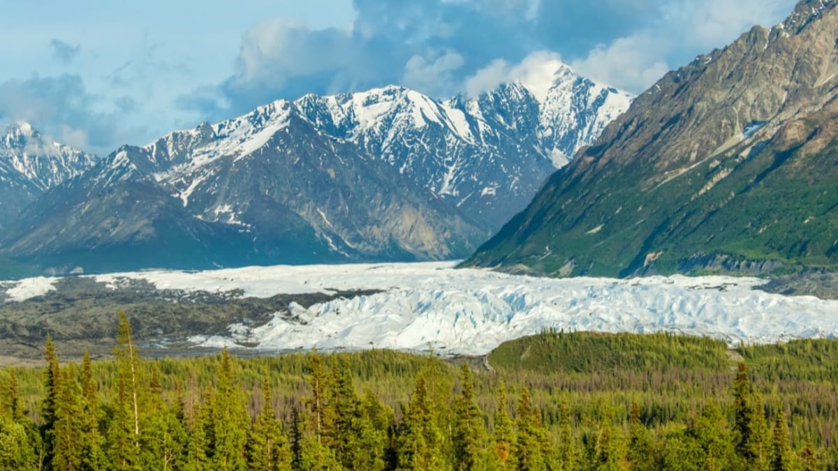 The ice of the Matanuska Glacier below snow-capped peaks and forest