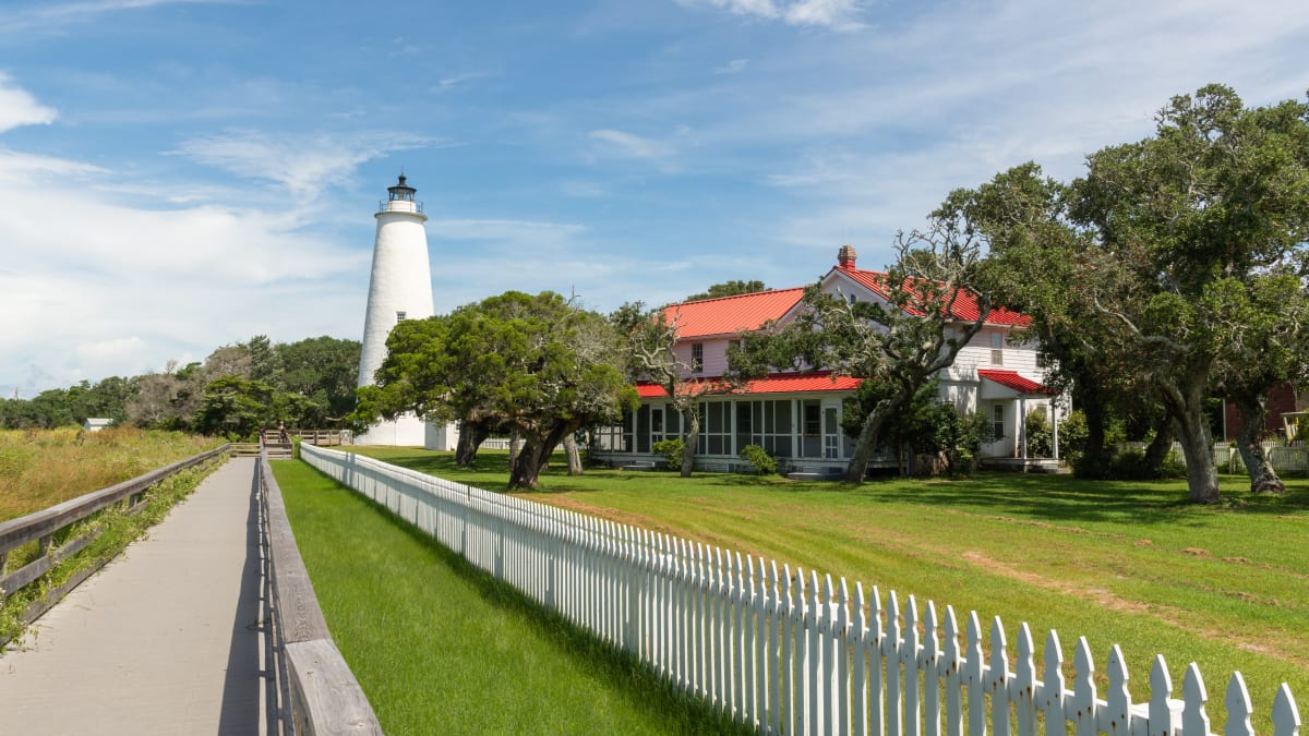 The short white Ocracoke Lighthouse and its red-roofed keeper's house behind a picket fence on Ocracoke Island, North Carolina