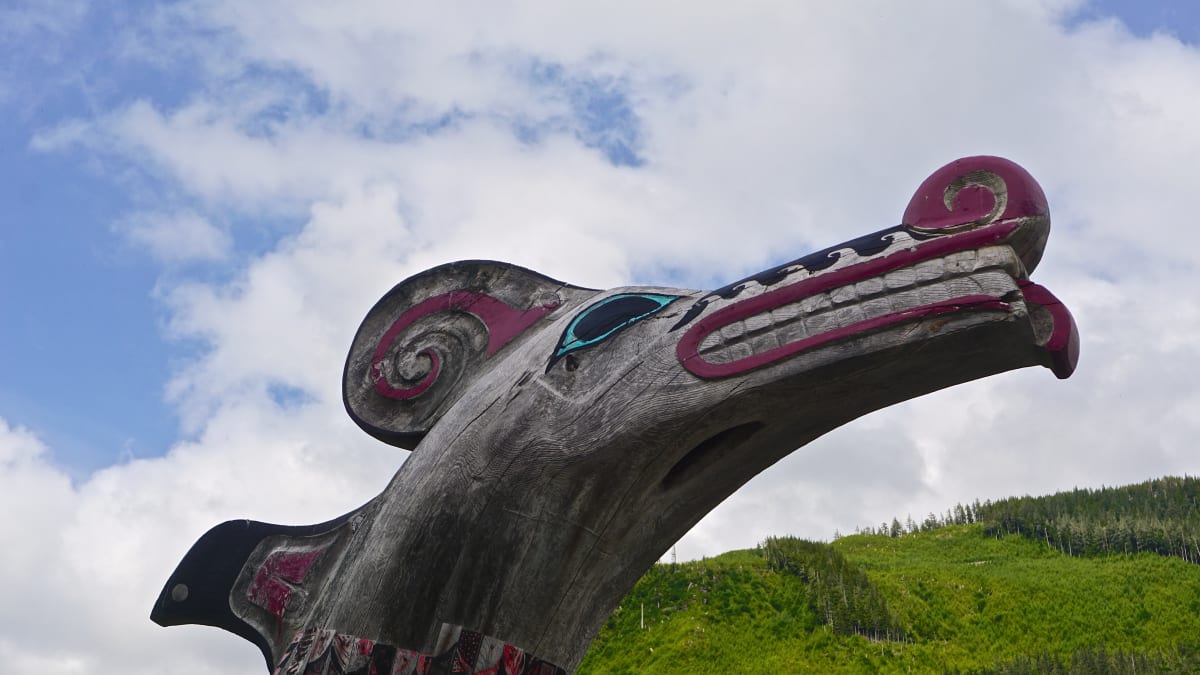 Hand-carved cedar totem poles and a clan house at Potlatch Totem Park north of Ketchikan, Alaska