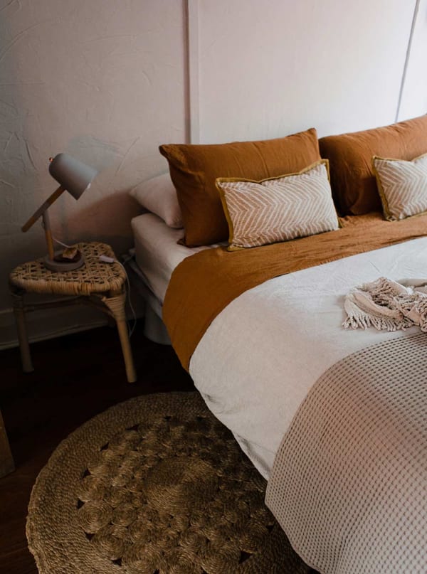 Warm terracotta boho boutique motel room with linen pillows, rattan nightstand, and woven rug