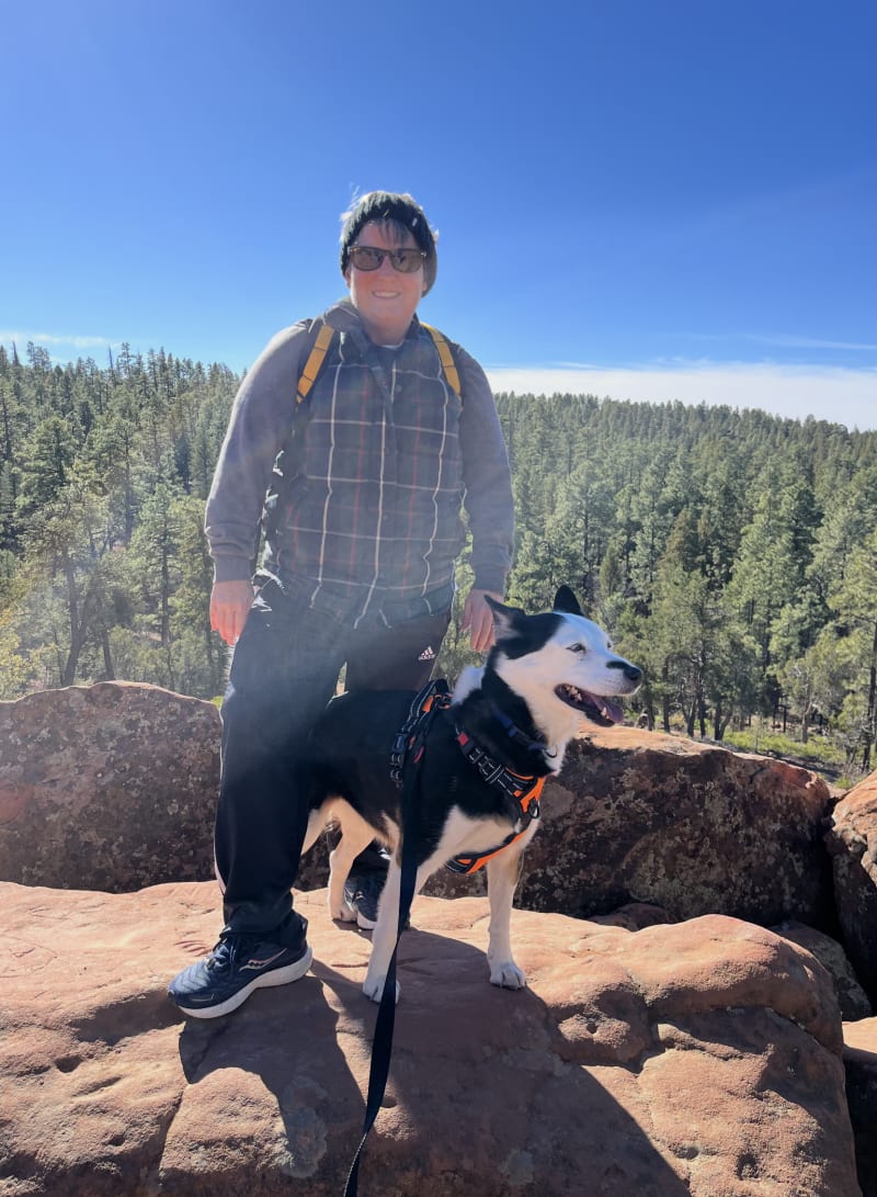 Boutels founder Sarah Powers hiking with her rescue dog Paige on a red-rock outcrop in an Arizona pine forest