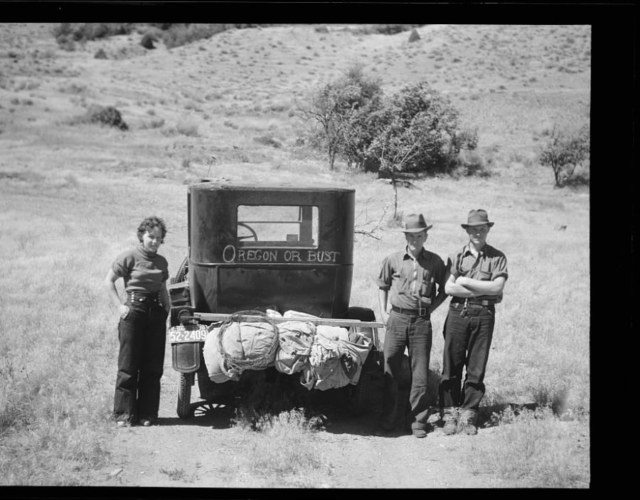A family stands beside their loaded Model T painted with 'Oregon or Bust' in Montana in 1936, leaving the drought-stricken plains for the Pacific Northwest