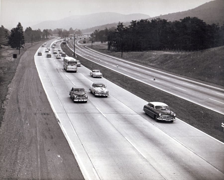 Black-and-white 1958 photo of the New York State Thruway, a divided interstate highway carrying cars between grassy shoulders