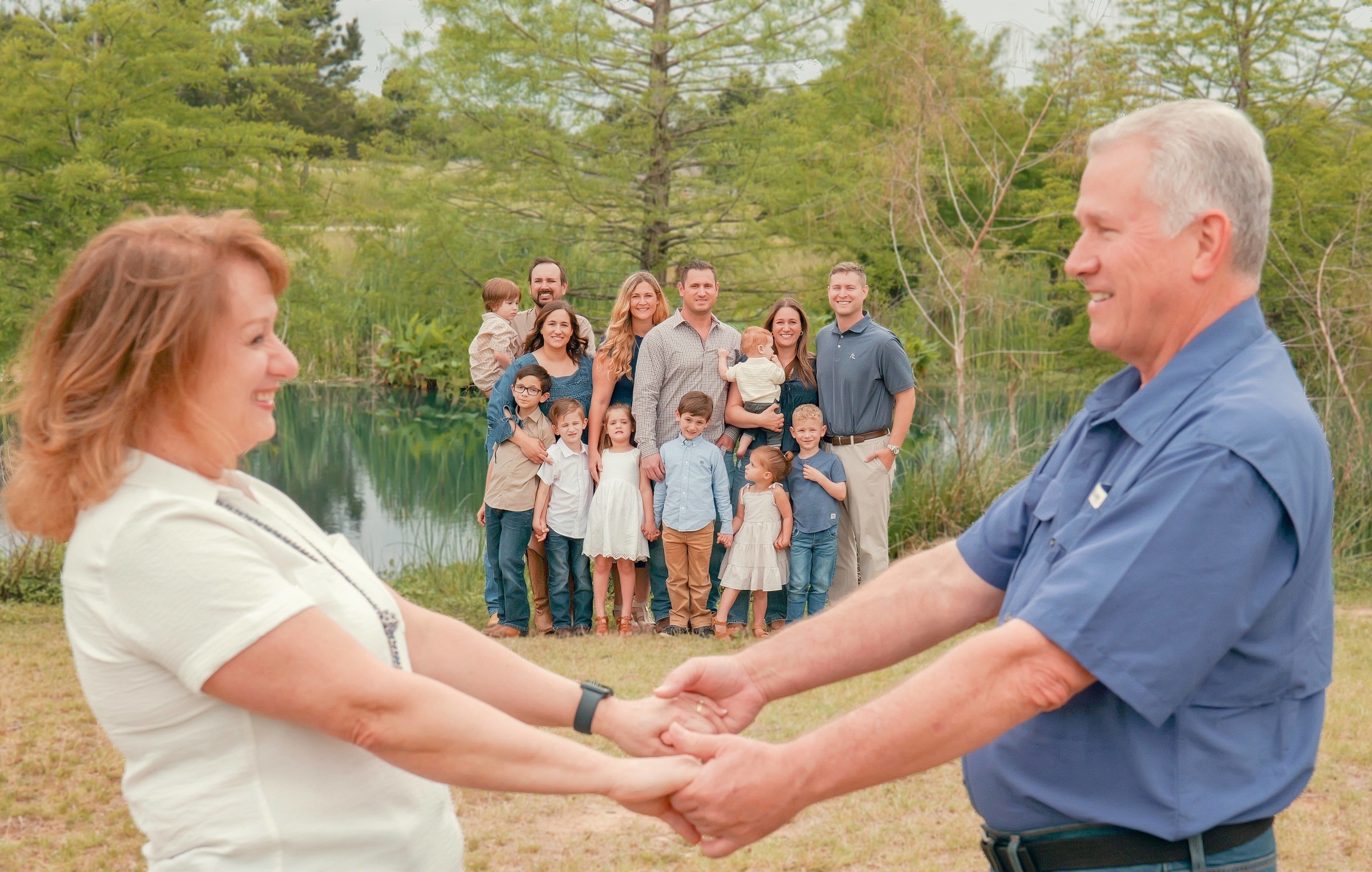 Grandparents holding hands with their extended family gathered behind them by a lake