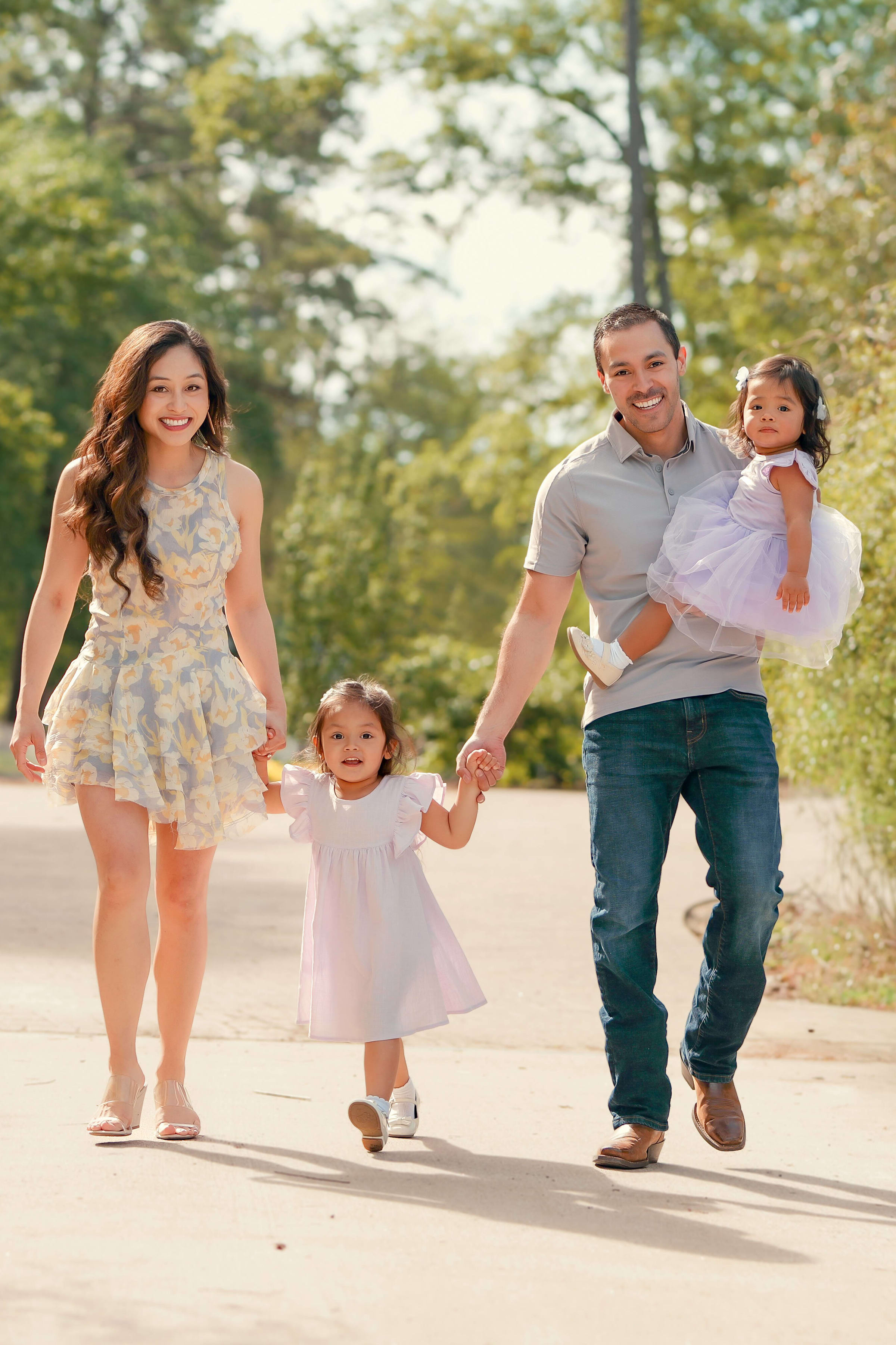 Parents walking with their two young daughters on a sunny tree-lined path