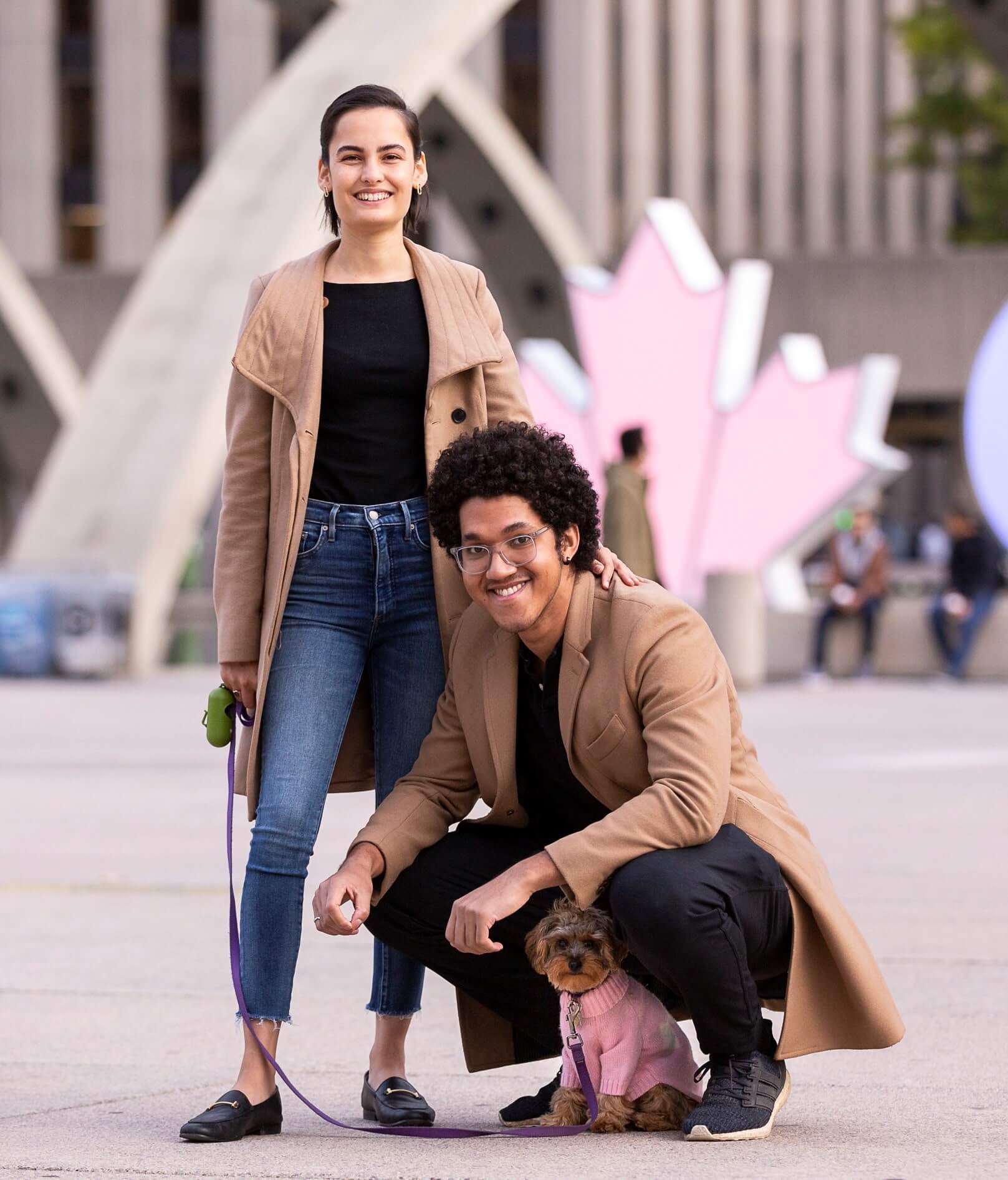 two people and their dog posing in front of a maple leaf sign