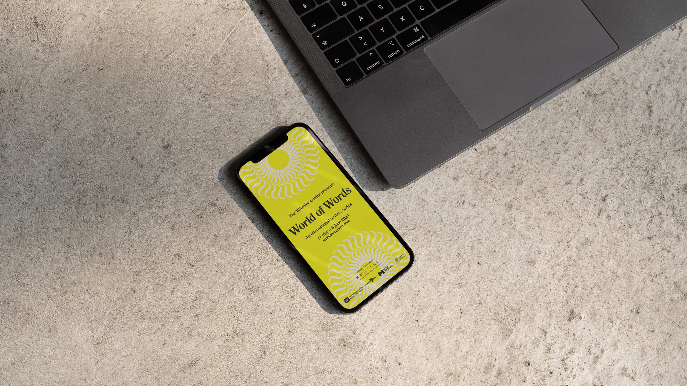 Over head view of mobile with a yellow screen sitting next to a laptop on a grey background. Text on mobile screen reads World of Words.