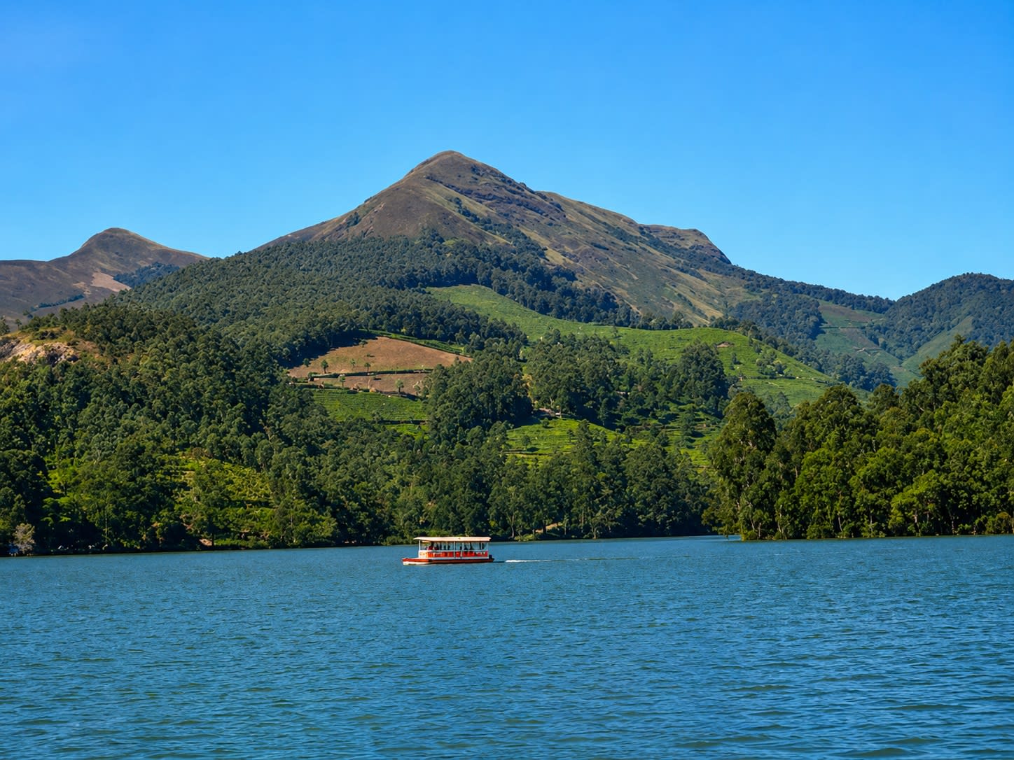 Boat cruising on Kundala Lake surrounded by green hills in Munnar, Kerala