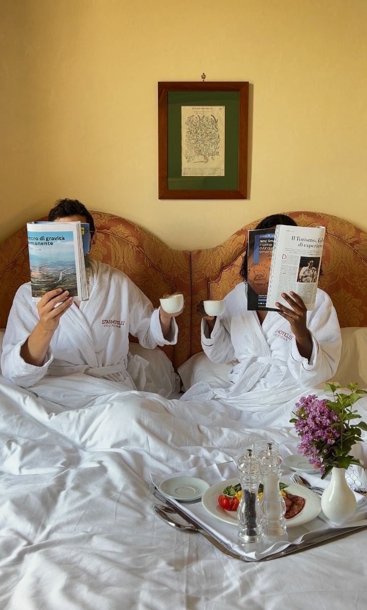 Two guests in hotel robes reading over breakfast in bed