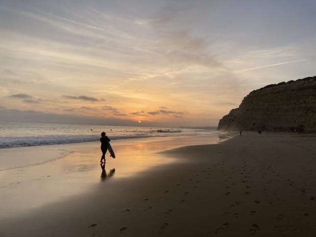 A surfer carrying their board along the shore at sunset