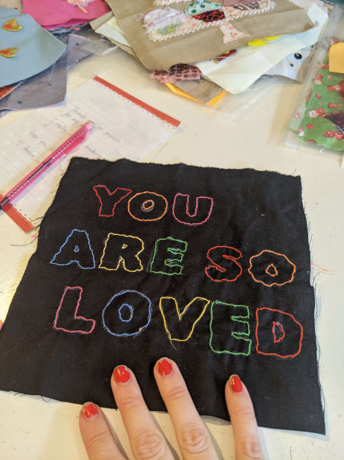 The words "you are so loved" embroidered on black fabric