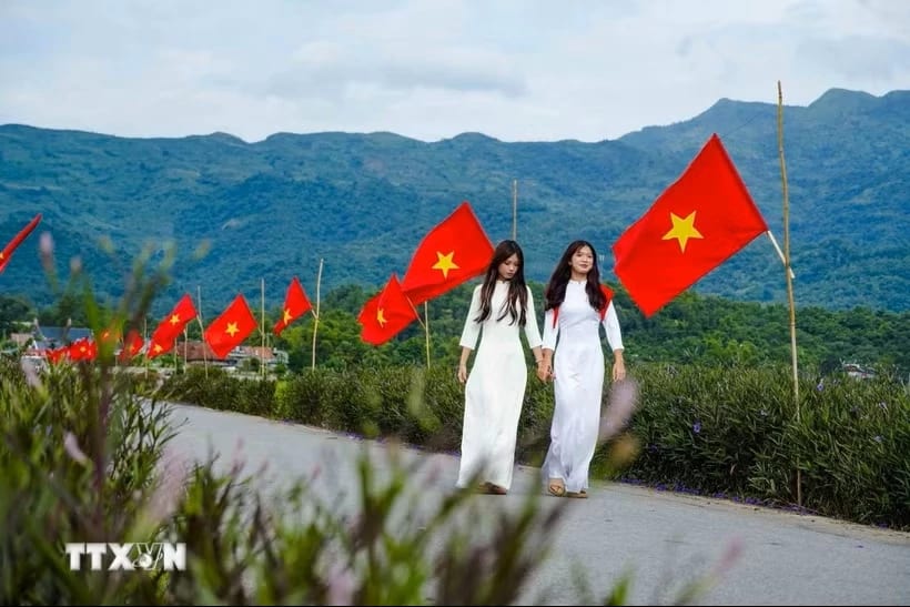 Hai nữ sinh trong trang phục áo dài giữa không gian rực rỡ cờ Tổ quốc trên cánh đồng Mường Thanh. (Ảnh: Xuân Tư/TTXVN)