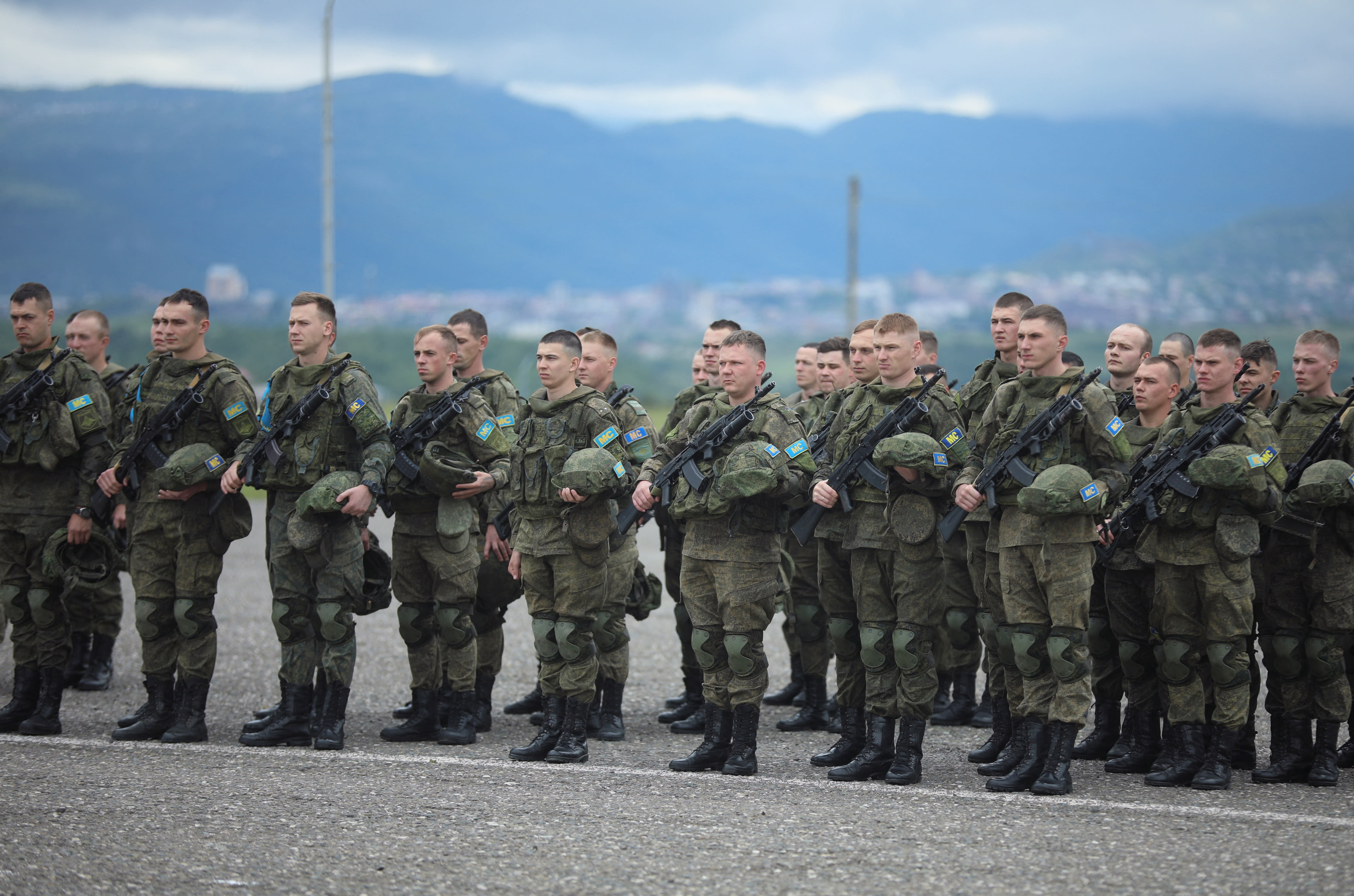 Soldiers stand at attention in front of mountains.