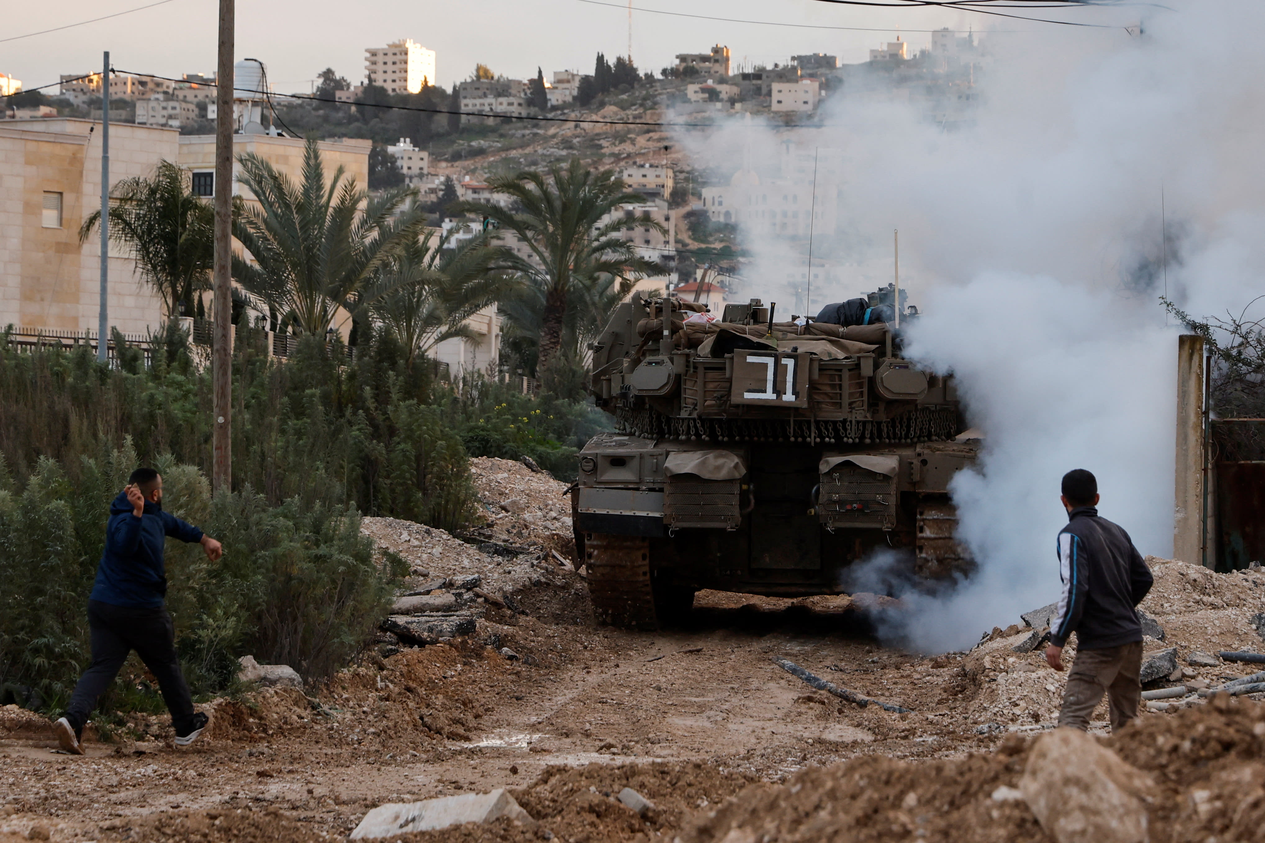 A man prepares to throw an object as an Israeli tank operates during an Israeli operation in Jenin, in the Israeli-occupied West Bank