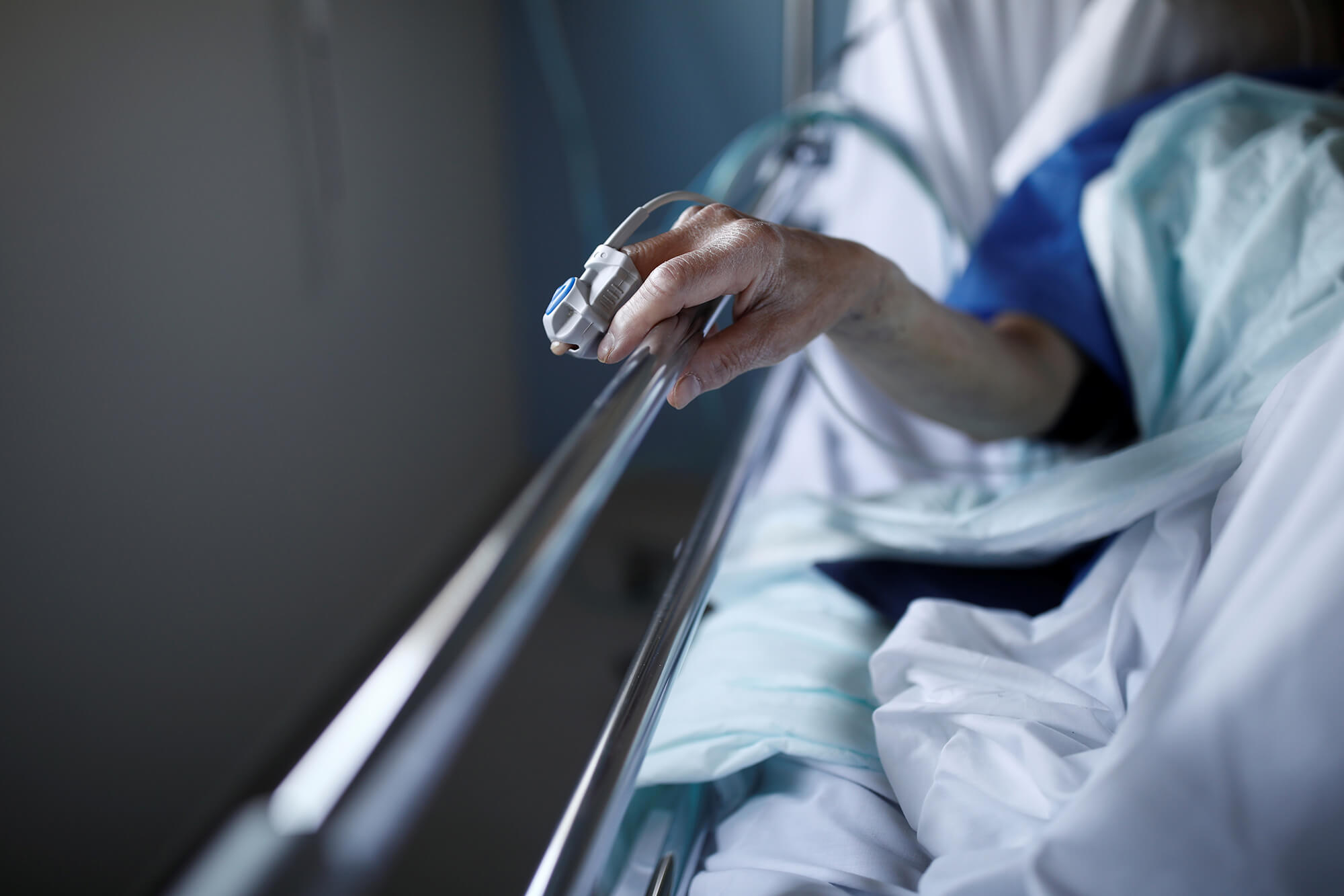 Photo of a hand with an oxygen monitor on a finger holding a bed rail.