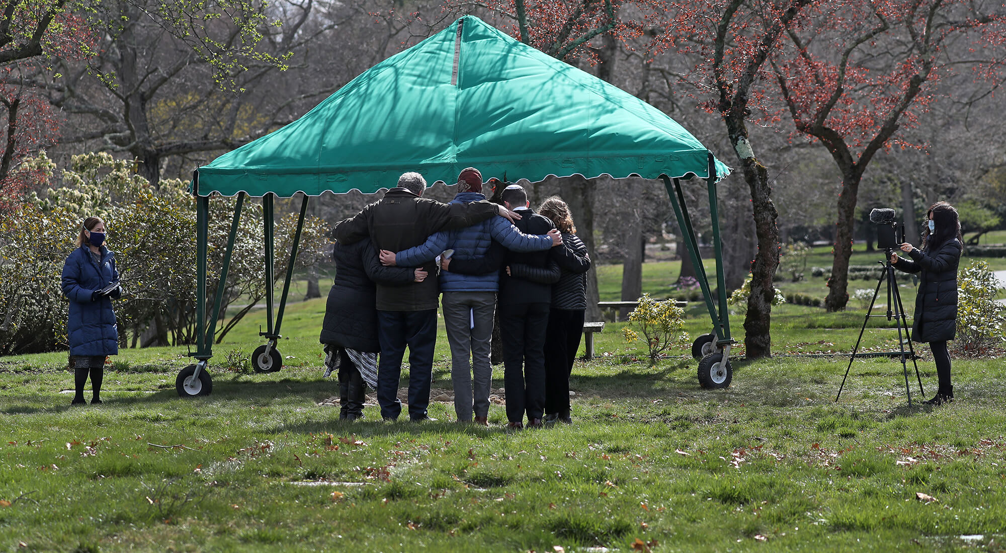 A group of mourners hugging in front of a green tent.