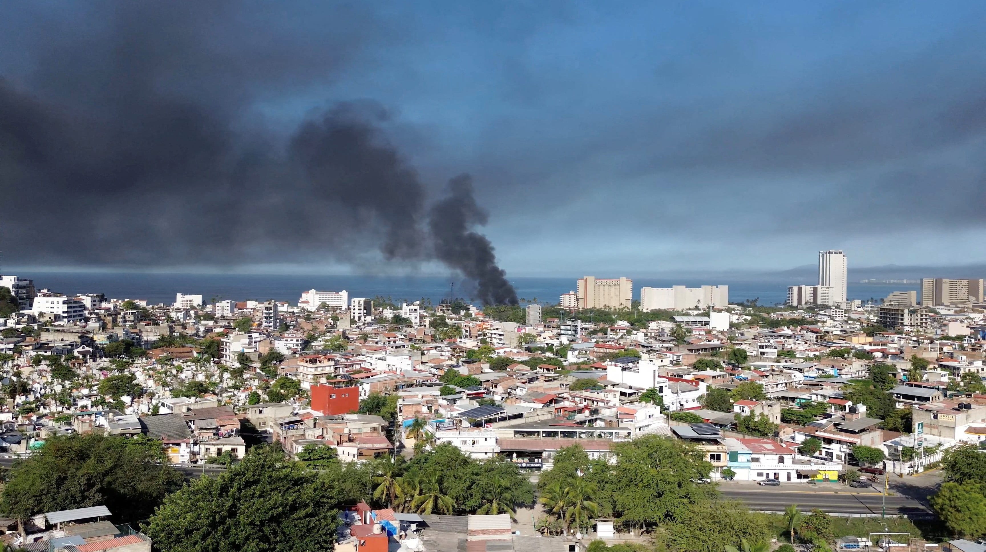 Smoke billows from an urban area by the sea.