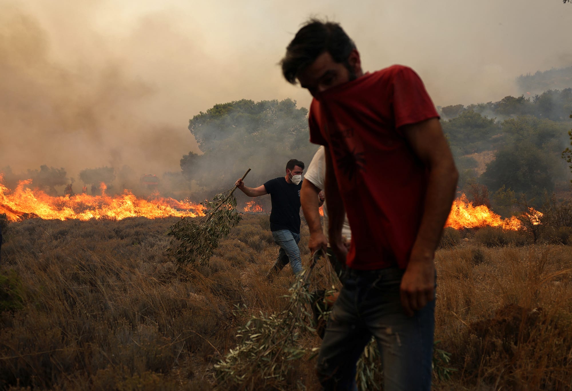 Tow men try to extinguish a wildfire burning near the village Vlyhada, near Athens, Greece