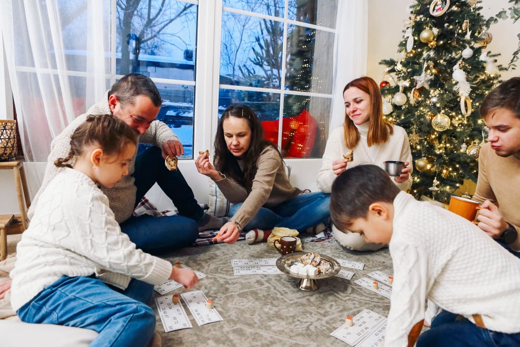 Big family with children sitting on floor near Xmas tree playing lotto board game together while spending leisure time at cozy home during Christmas holidays. Indoor winter activities