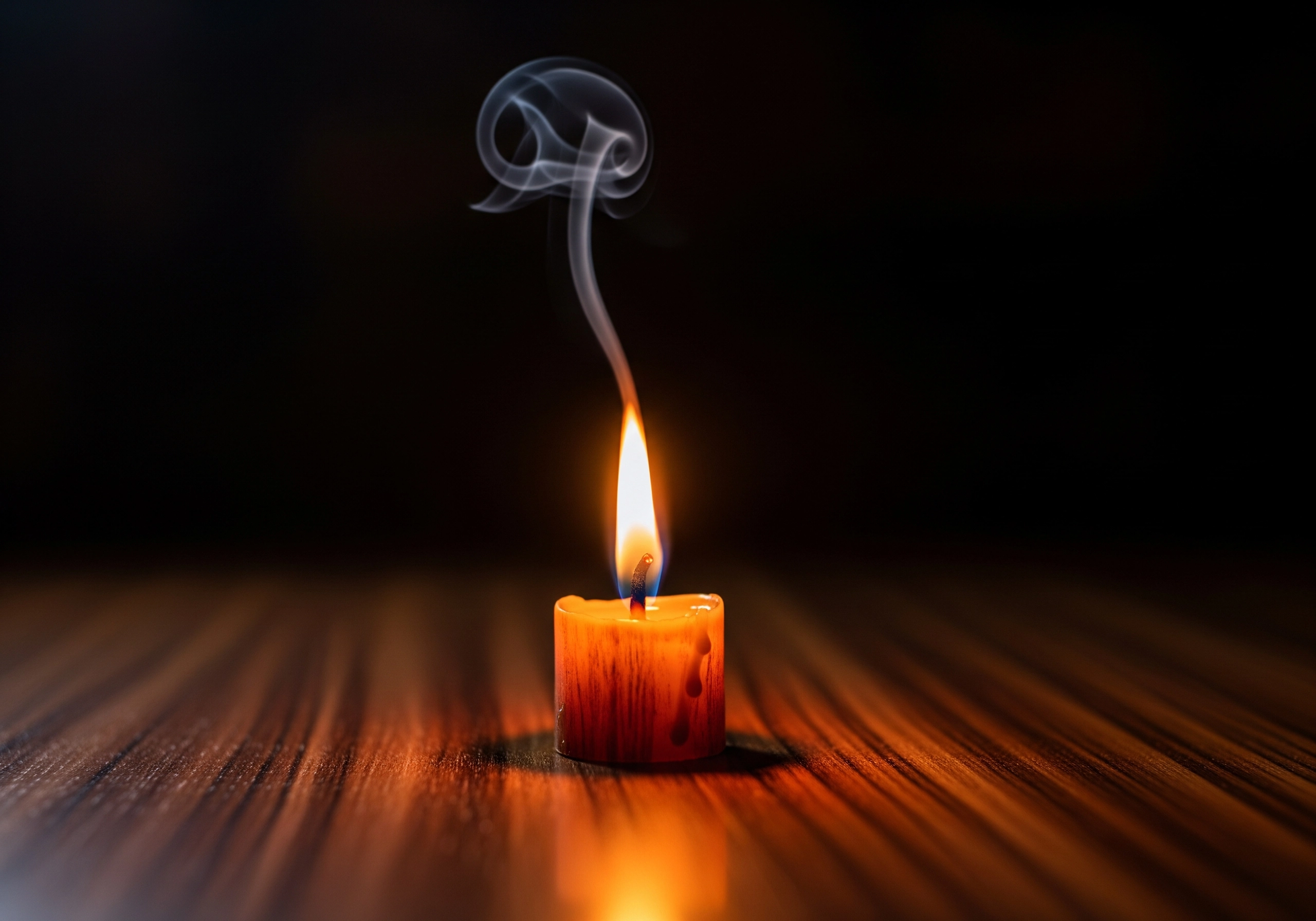 Lit candle with swirling smoke on a dark wooden surface.
