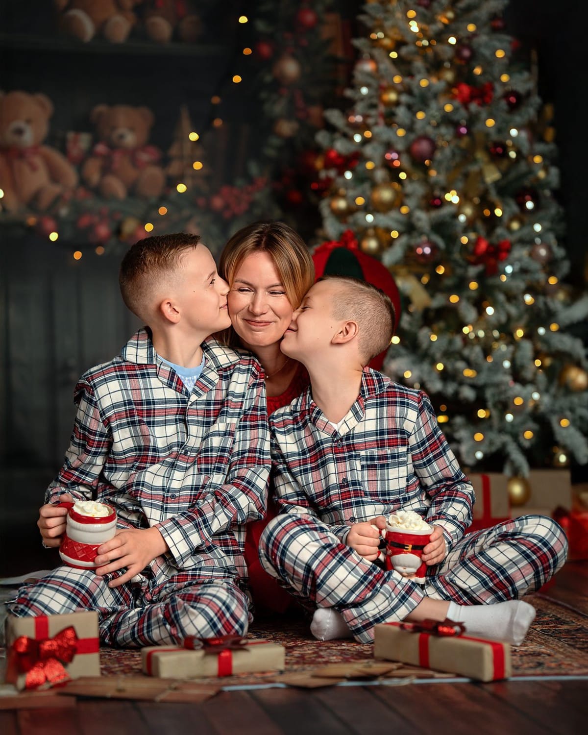 Mama z dwoma chłopcami w piżamach w kratkę całują się podczas świątecznej sesji rodzinnej.