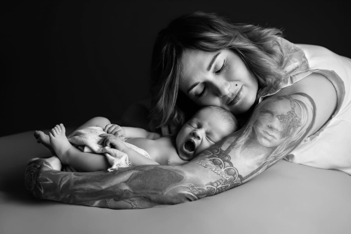 Mama z noworodkiem na sesji noworodkowej, czarno-białe zdjęcie, delikatne światło, czułość i bliskość.