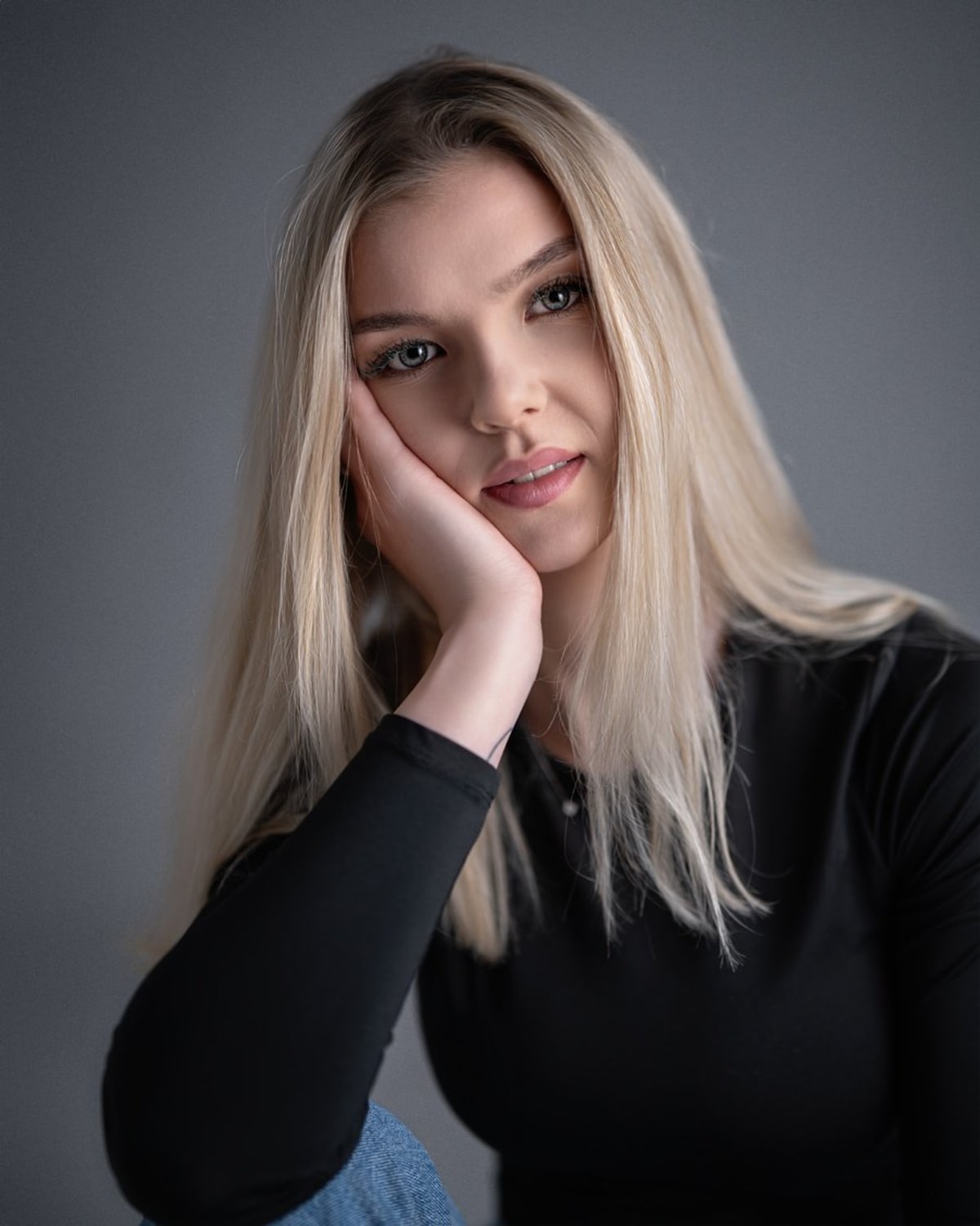 Portret nastolatki w czarnym swetrze, długie jasne włosy, ręka przy twarzy, naturalne światło.
