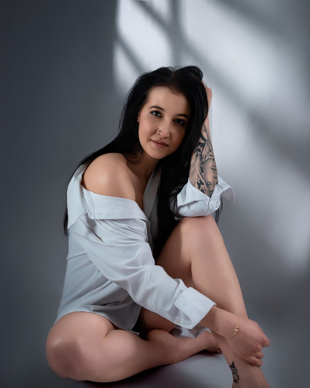 Dorosła kobieta w białej koszuli pozuje do sesji fotograficznej z artystycznym oświetleniem.
