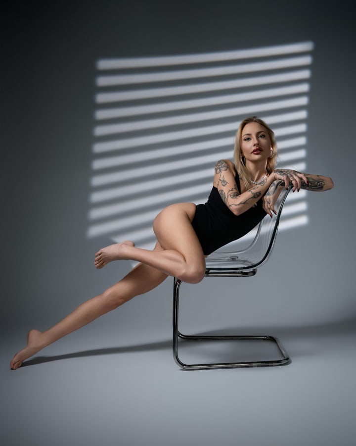 Woman in black bodysuit on metal chair, dynamic pose, natural striped light creating geometric shadows, sensual session.