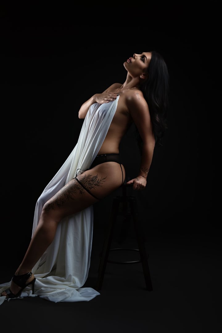 Woman in white draped fabric during sensual photography session against black background.
