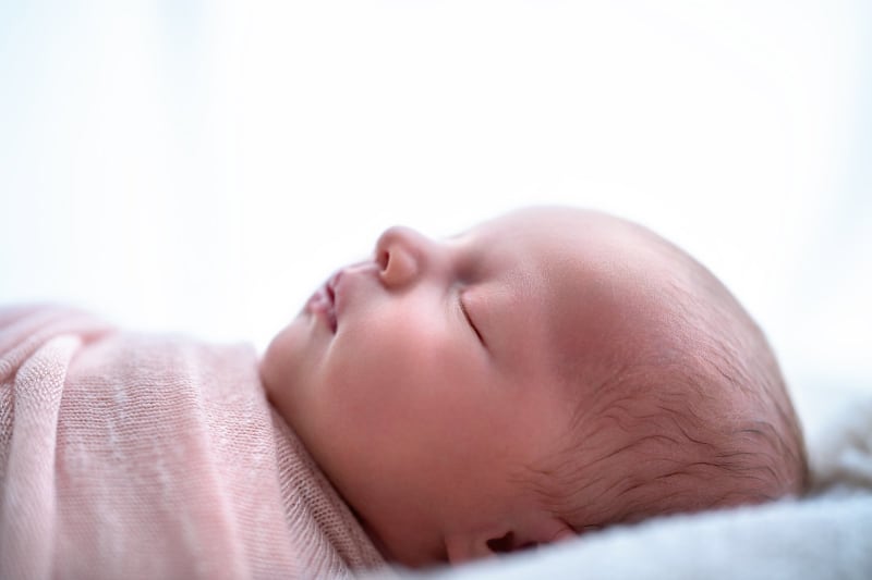 Śpiący noworodek owinięty w różowy koc podczas sesji noworodkowej, delikatne światło