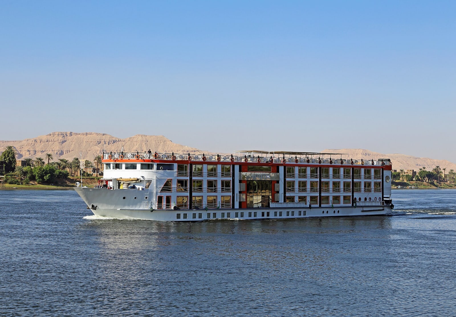A Nile cruise boat moored on the river at Luxor with palms along the bank