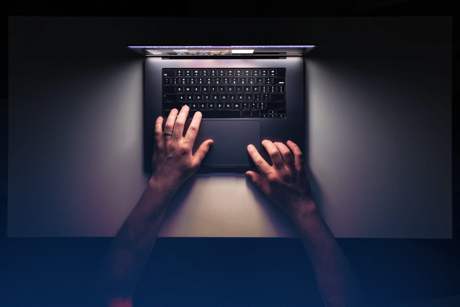 Vista aérea de uma pessoa sentada em frente a um notebook com as mãos sobre a mesa e sobre o notebook