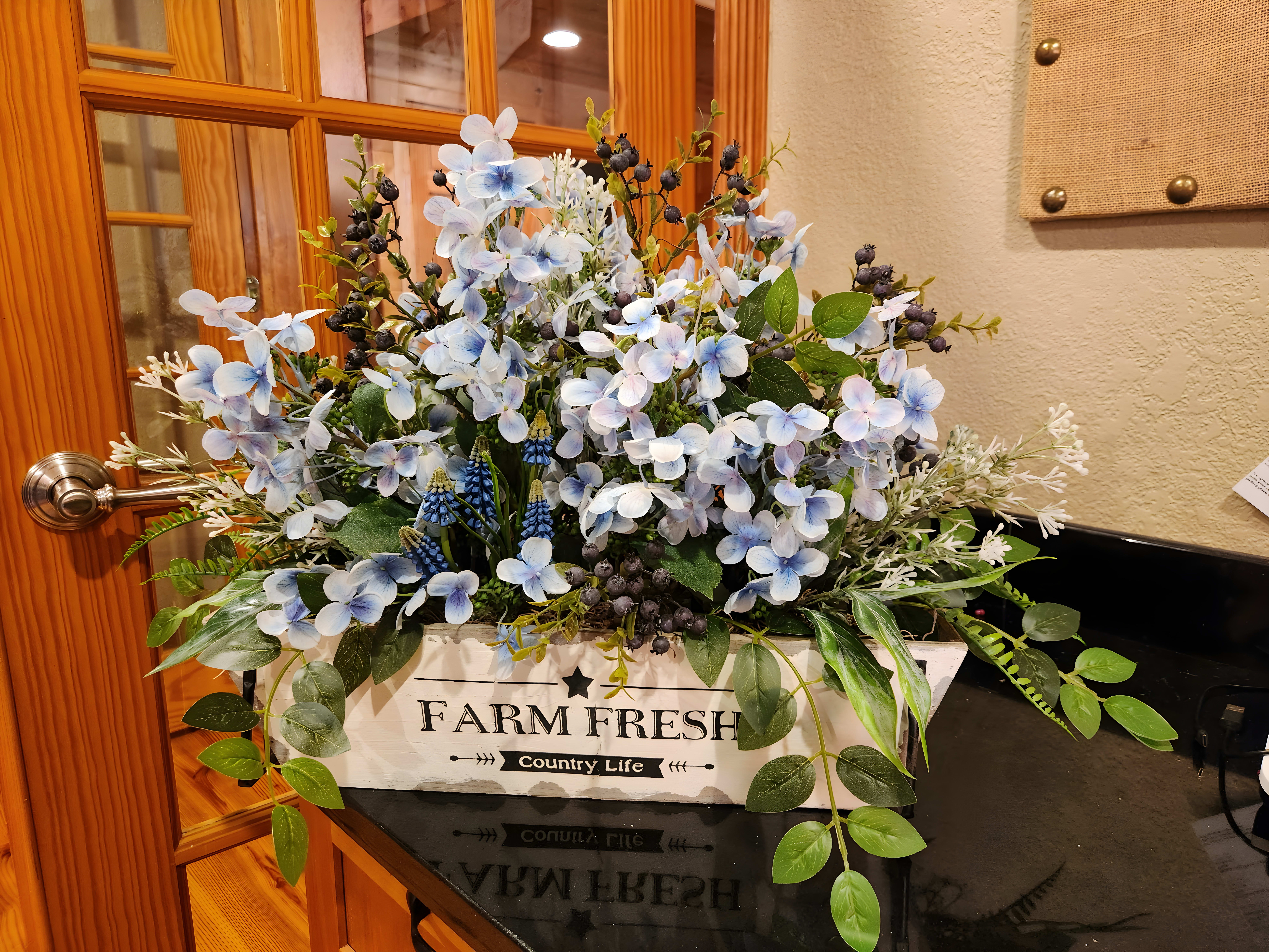 Forest arrangement with white flowers and pinecones with a sign that says 'FARM FRESH COUNTRY LIFE' in the middle