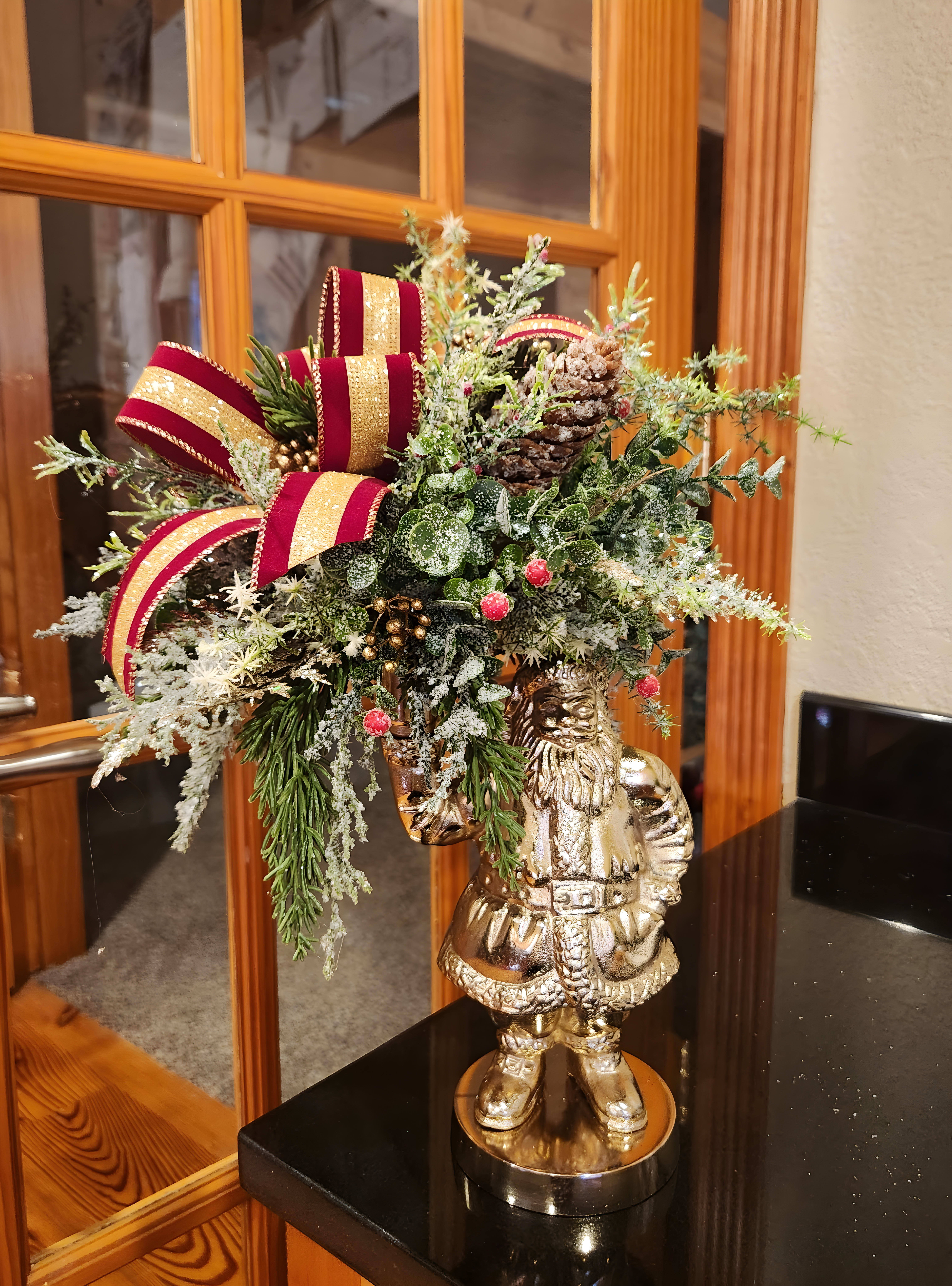 Winter forrest arrangement with a red and yellow ribbons being held up by a Santa statue
