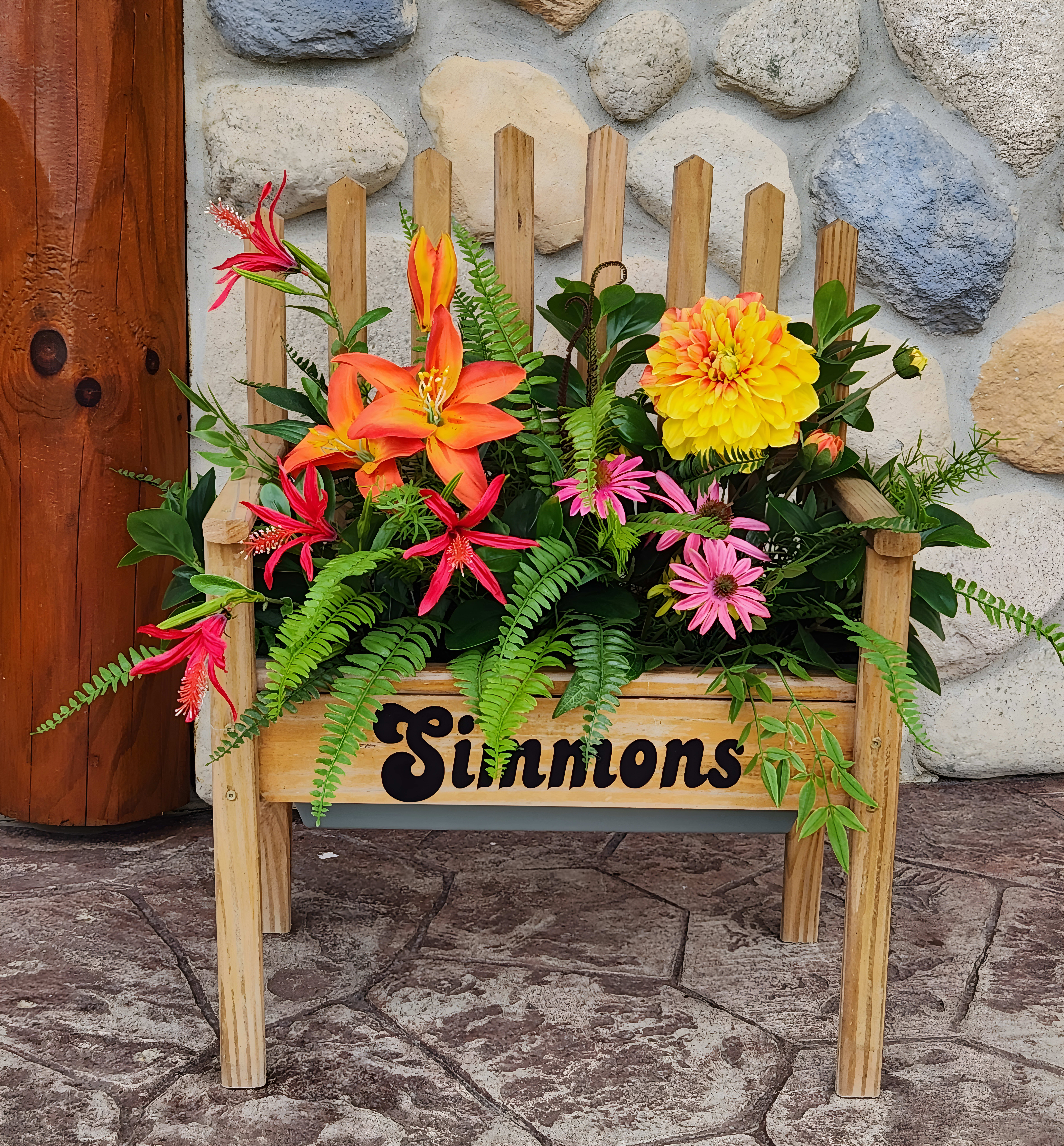 Pink, red, reddish-pink, and yellow flowers on a bench that says 'Simmons' in the middle