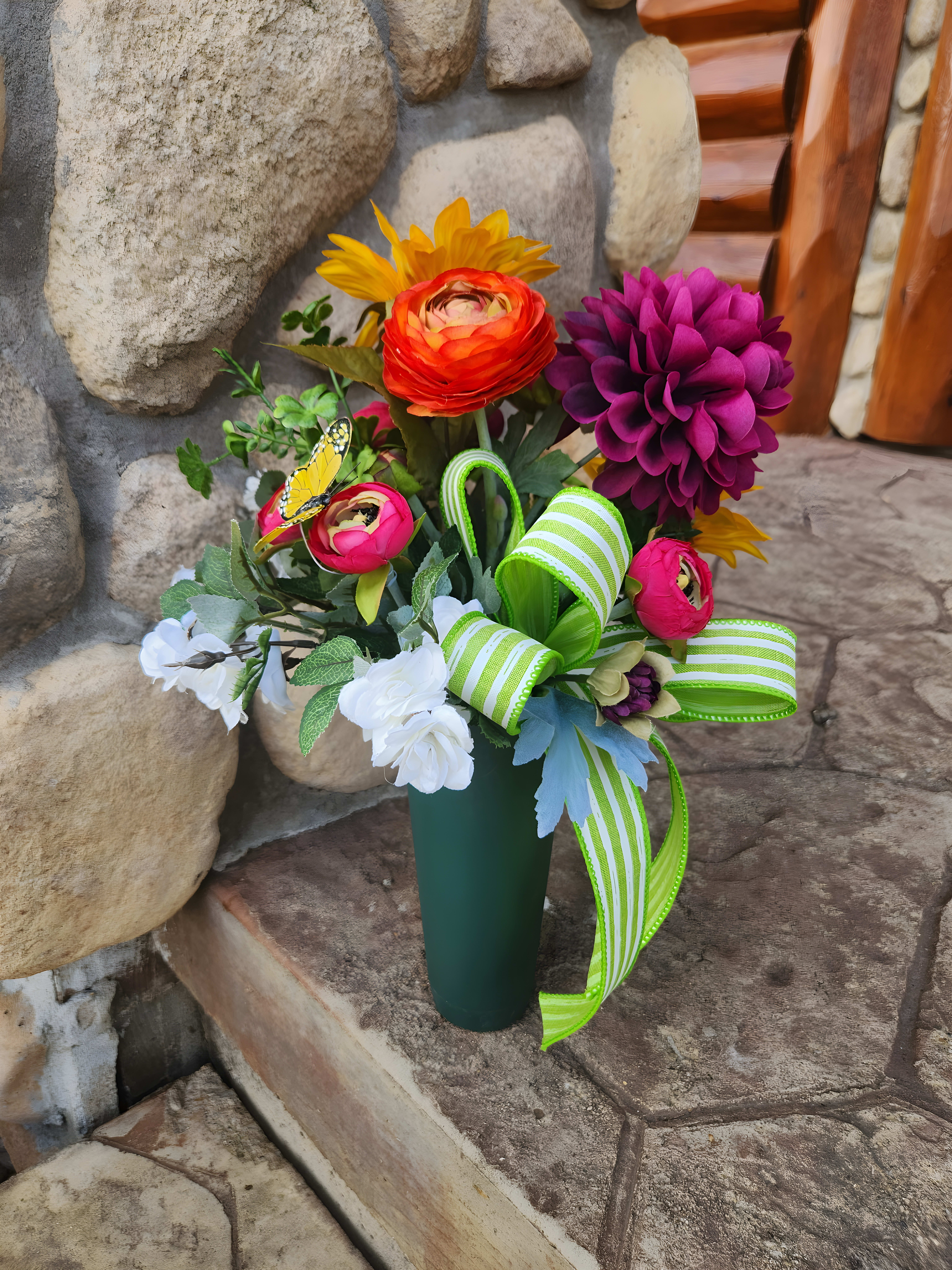 Red, pink, purple, dark-yellow, and white flowers in a green vase with a light green plaid ribbon