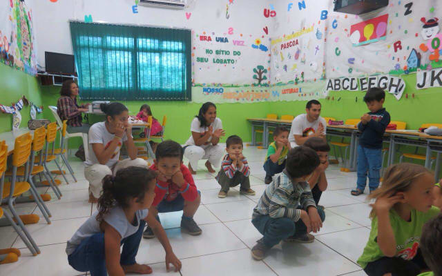 Children practicing capoeira movements together in a classroom