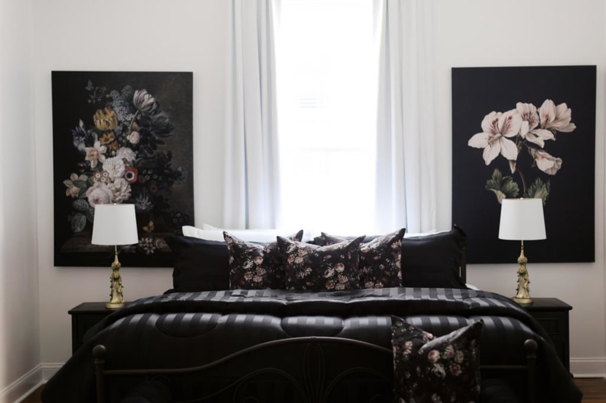 The Master bedroom: black iron four-poster, dramatic floral canvases, gold lamps, striped duvet