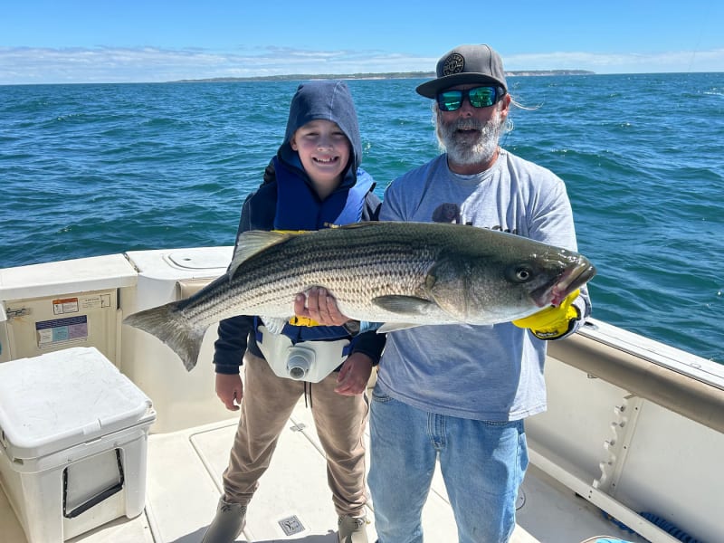 Young angler and Captain Matt King holding a striped bass with Block Island in the background