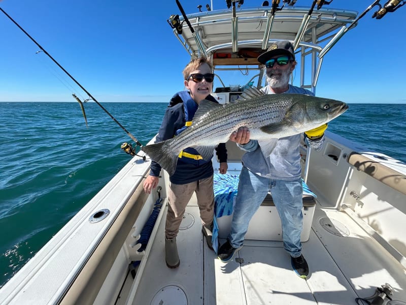 Young angler and Captain Matt King holding a large striped bass aboard the Hula Dog