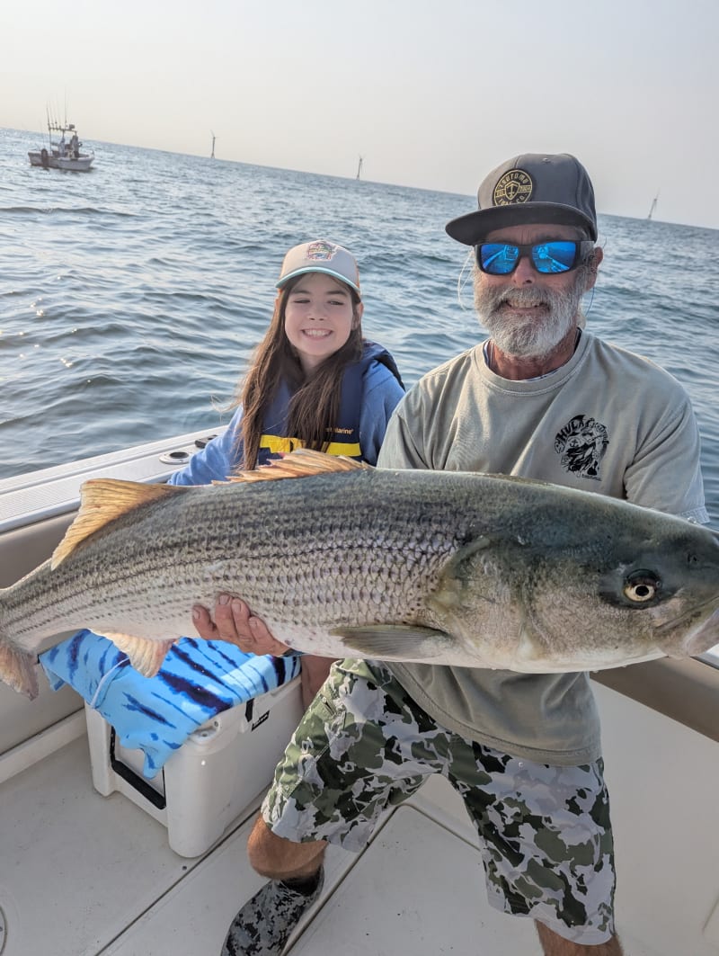 Young girl and Captain Matt holding a striped bass aboard the Hula Dog