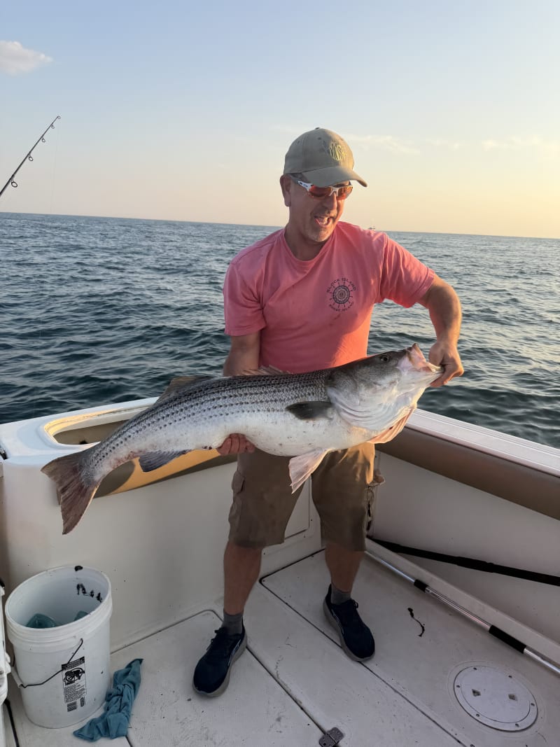 Angler in a pink shirt holding a striped bass at sunset aboard the boat off Block Island