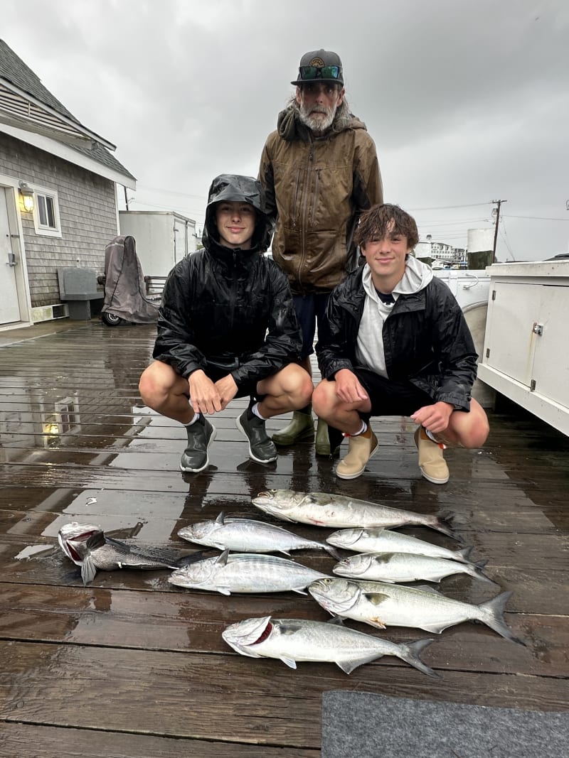 Two young anglers and a crew member on a wet Old Harbor dock with a spread of bluefish and a striped bass caught aboard the Hula Dog off Block Island