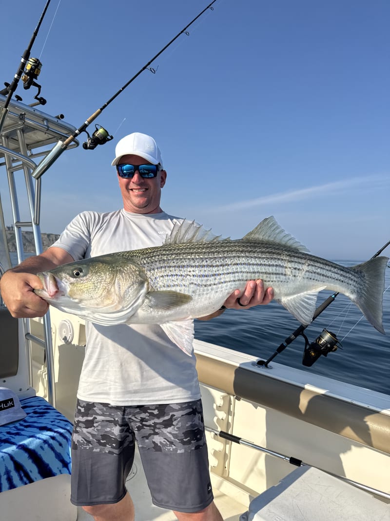 An angler holding a personal-best striped bass aboard the Hula Dog
