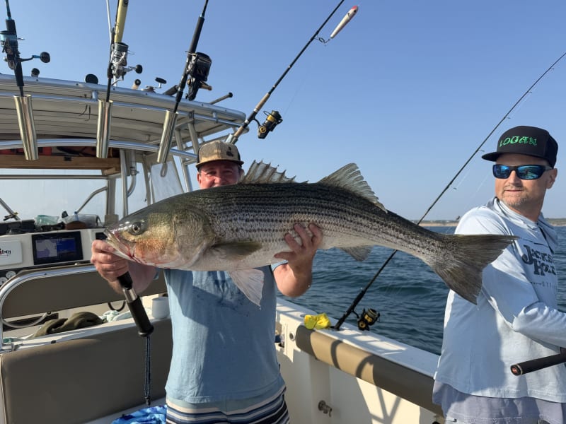 Two anglers aboard the boat, one holding a striped bass off Block Island
