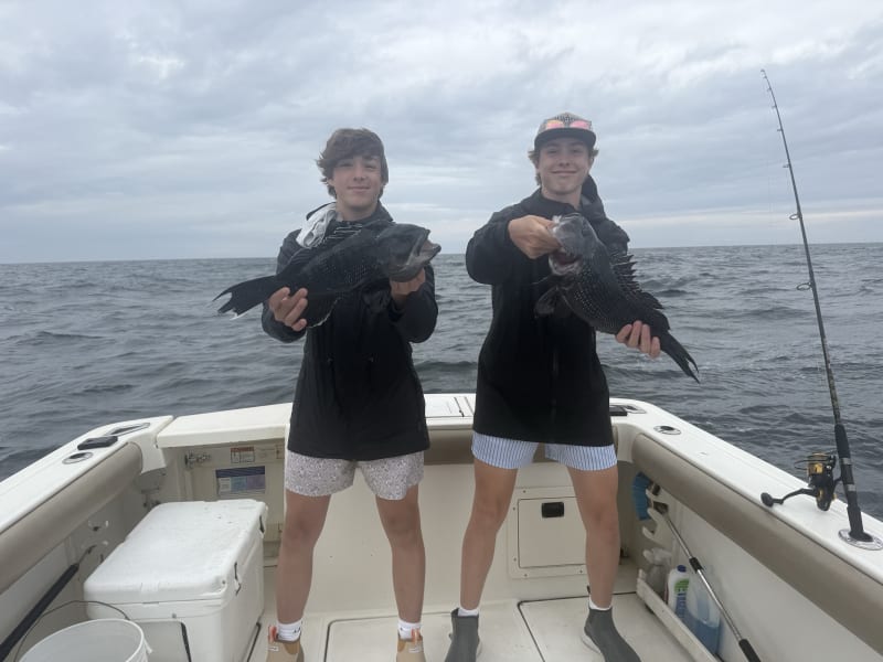 Two young anglers each holding a large black sea bass aboard the Hula Dog on an overcast day off Block Island