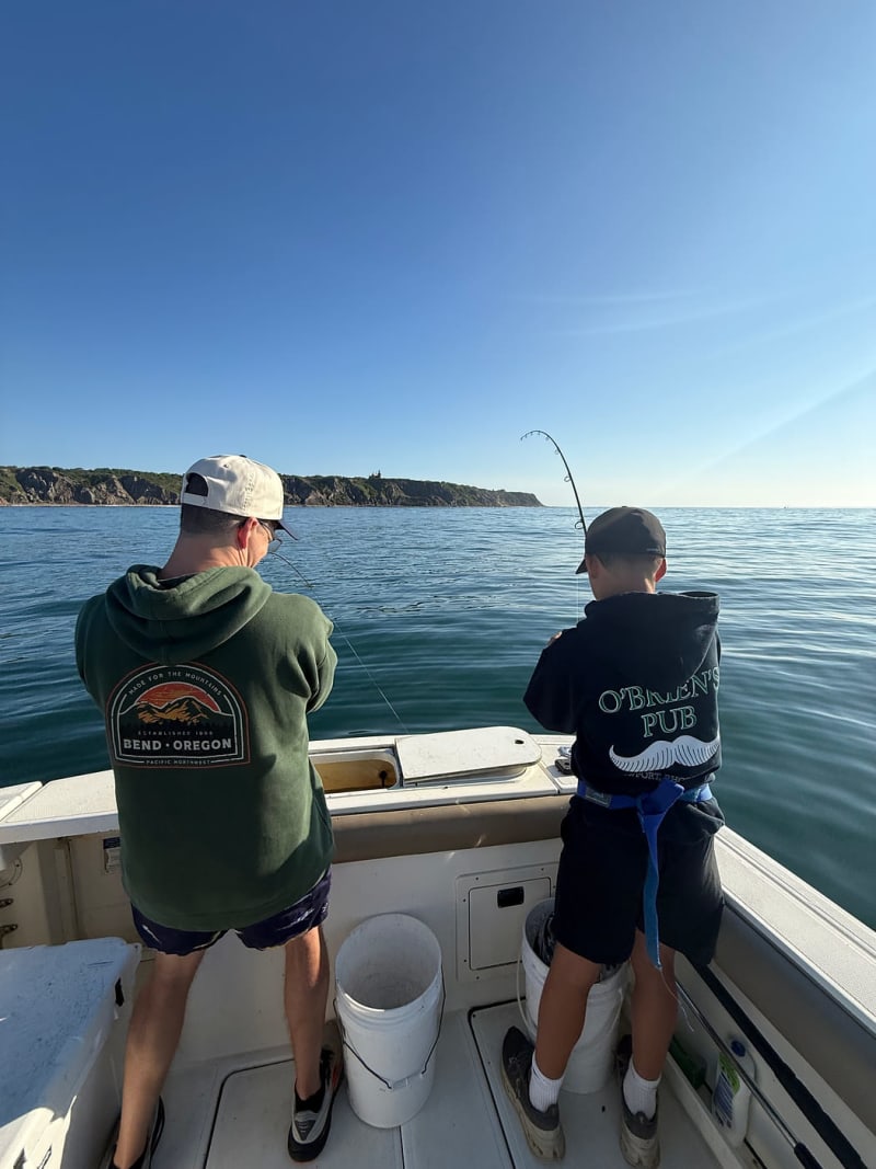 Two young anglers fishing off the stern of the Hula Dog with Block Island in the background